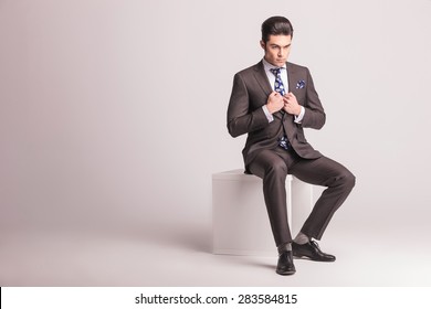 Full body picture of a young elegant business man sitting on a white chair while pulling his collar.