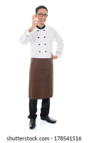 Full Body Portrait Of Asian Chef Showing Tasty And Satisfied Hand Sign , Smiling And Standing Isolated On White Background.