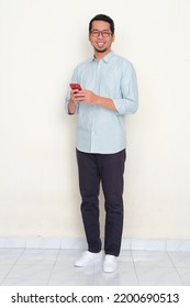 Full Body Portrait Of Asian Man Smiling To Camera While Using His Mobile Phone