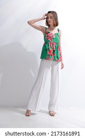 Full Body Portrait Of A Brunette Young Woman In Summer Floral Pattern Print. Shirt, With White Pants

