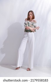 Full Body Portrait Of A Brunette Young Woman In Summer Floral Pattern Print. Shirt,with White Pants, With Palm Shadow

