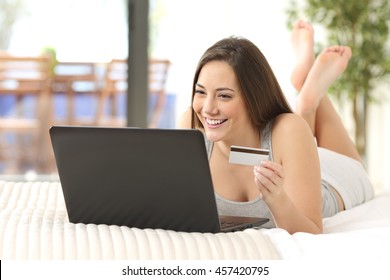 Full body portrait of a casual female buying on line lying on a bed of an hotel room or home