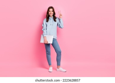 Full body portrait of cheerful pretty lady hold netbook demonstrate v-sign isolated on pink color background