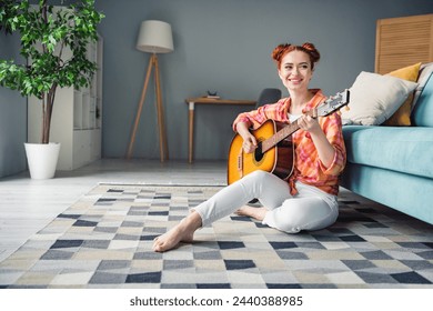 Full body portrait of cheerful pretty lady sit floor enjoy play guitar spend free time modern apartment inside - Powered by Shutterstock