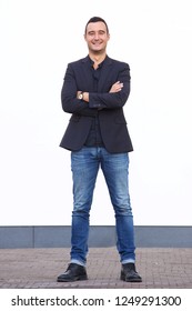 Full Body Portrait Of Confident Man Standing Against White Wall With Blazer And Jeans