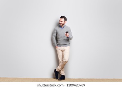 Full Body Portrait Of Cool Businessman Holding Cellphone Against Gray Wall