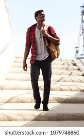 Full Body Portrait Of Cool Young Man With Bag Walking Down The Steps And Looking Away