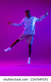 Full Body Portrait Of Ecstatic African Man Jumping In Modern Neon Light Studio Background