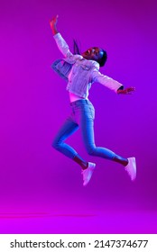 Full body portrait of ecstatic African-American woman jumping in modern neon light studio background