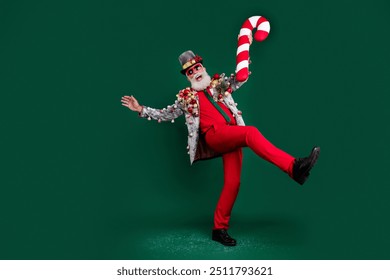 Full body portrait of excited aged man festive ornament outfit dance big candy stick isolated on dark green color background - Powered by Shutterstock