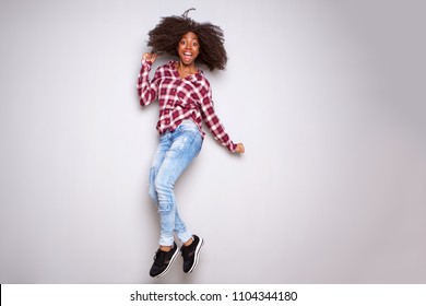 Full body portrait of excited young black woman jumping with joy over white background