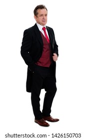 Full Body Portrait Of Handsome Confident Caucasian Mature Businessman 55-60 Years Old In Black Tuxedo And Red Vest Standing With Hand In Pocket On Isolated White Background.