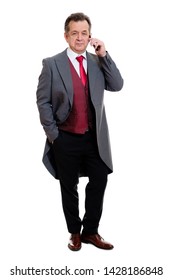 Full Body Portrait Of Handsome Confident Caucasian Mature Businessman 55-60 Years Old In Grey Tuxedo And Red Vest. Rich Senior Man Talk By Phone And Looking To Camera On Isolated White Background