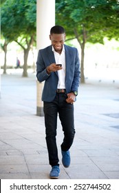 Full Body Portrait Of A Handsome Man Walking And Sending Text Message On Cellphone