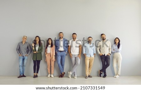 Full body portrait of happy business people in smart and casual clothes. Full length group of senior and young Caucasian men and women posing against grey studio wall. Clothing and fashion concept