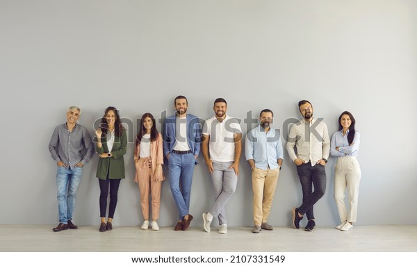 Full body portrait of happy business people in
smart and casual clothes. Full length group of senior and young
Caucasian men and women posing against grey studio wall. Clothing
and fashion concept