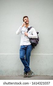 Full Body Portrait Of Happy Man Talking With Mobile Phone By Gray Wall