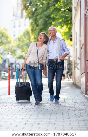 Full body portrait happy older couple walking with suitcase on street