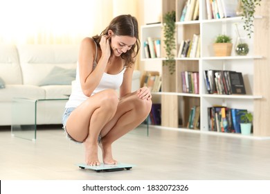 Full body portrait of a happy woman measuring weight with scale at home