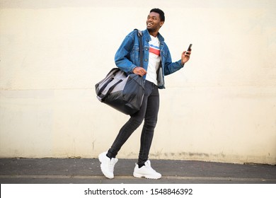 Full Body Portrait Of Happy Young African American Man Walking With Bag And Mobile Phone On Street