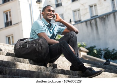 Full body portrait happy young black man sitting on steps in city talking with cellphone  - Powered by Shutterstock