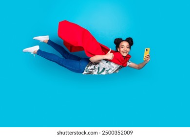 Full body portrait of lovely young girl superhero costume fly smart phone thumb up isolated on blue color background - Powered by Shutterstock