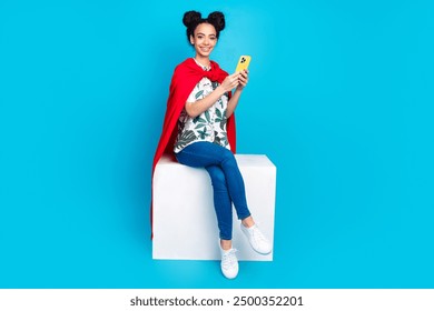 Full body portrait of lovely young girl superhero costume sit podium use phone isolated on blue color background - Powered by Shutterstock