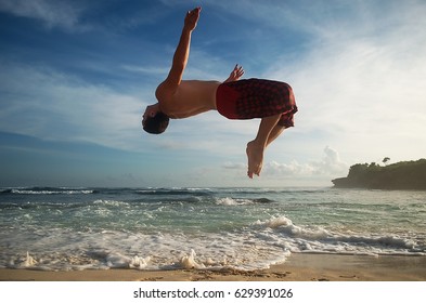 Full Body Portrait Of Parkour Man Jumping High On The Beach Performing A Back Flip