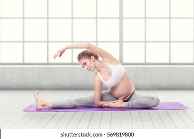 Full Body Portrait Of Pregnant Woman Doing Yoga On a Purple Exercise Mat in front of a large window - Powered by Shutterstock