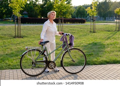 Full Body Portrait Of Senior Woman 60-65 Years Old On Bicycle. Older Lady Riding City Bike In European Town. Old Smiling Female Cycling With Her Bike In Summer Time.