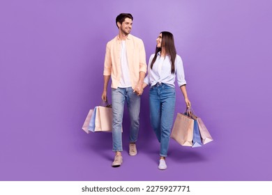 Full body portrait of two idyllic nice people hold hands walk store mall packages isolated on purple color background