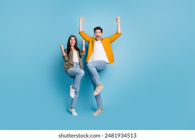 Full body portrait of two young people rejoice raise fists wear shirt isolated on blue color background - Powered by Shutterstock