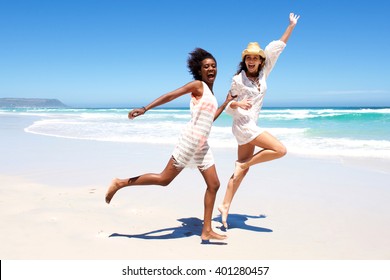 Full body portrait of two young women friends laughing and running on the beach