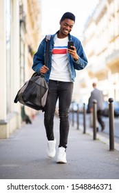 Full Body Portrait Of Young African American Man Walking With Mobile Phone And Bag In City