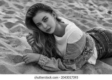 Full Body Portrait Of Young Beautiful Fashionable Woman Posing On The Sand. Model Wearing Blue Denim Jacket, Jeans, Top, Cowboy Boots. Female Fashion Concept