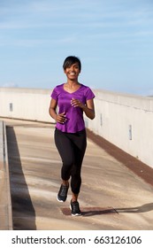 Full Body Portrait Of Young Black Woman Jogging Outdoors And Smiling