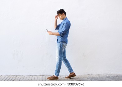 Full Body Portrait Of A Young Man Walking And Reading Text Message On Cell Phone