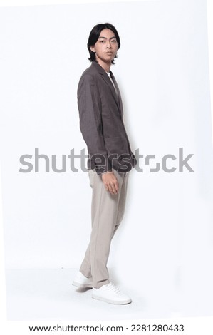 Full body portrait of young man wearing brown suit, with khaki pants posing on white background,