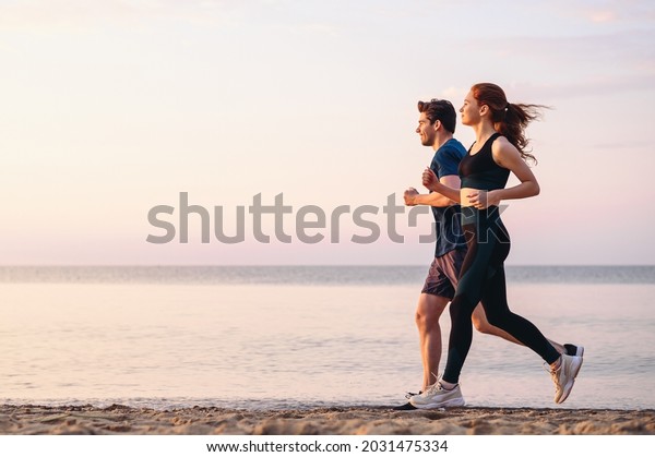 Full body profile couple young two friends strong\
sporty sportswoman sportsman woman man 20s in sport clothes warm up\
training run on sand sea ocean beach outdoor jog on seaside in\
summer day morning