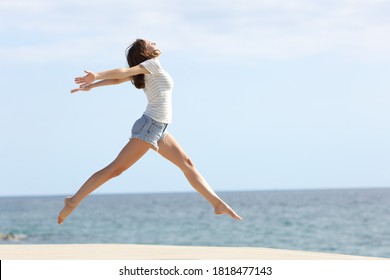 Full body profile of a happy woman with long waxed legs jumping on the beach