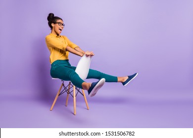 Full Body Profile Photo Of Amazing Dark Skin Lady Sitting On Chair Between Legs Like Driving Car Wear Specs Yellow Shirt Trousers Isolated Purple Color Background