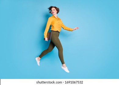 Full body profile photo of beautiful business lady jumping high up hold notebook going conference wear yellow shirt green pants shoes isolated bright blue color background