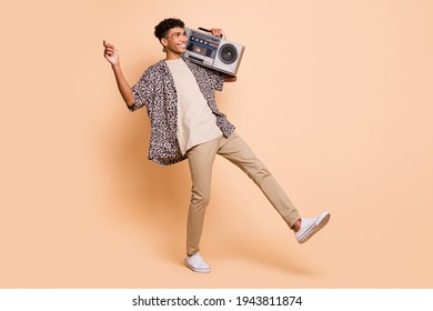 Full body profile photo of carefree dark skin guy hold boombox look empty space isolated on beige color background