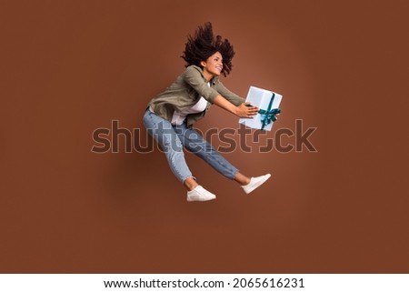 Full body profile photo of carefree energetic girl arms hold giftbox toothy smile isolated on brown color background