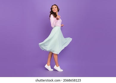 Full body profile photo of cool young brunette lady go look empty space wear shirt skirt sneakers isolated on purple background