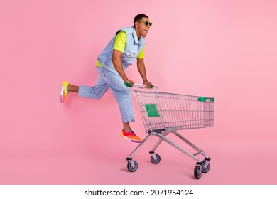 Full body profile photo of cool young brunet guy run do shopping wear eyewear t-shirt vest jeans sneakers isolated pink background