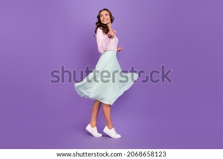Full body profile photo of cool young brunette lady go look empty space wear shirt skirt sneakers isolated on purple background