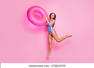 Full body profile photo of crazy funny lady fit legs long straight hairdo jump high into water hold hands big life buoy wear striped bodysuit isolated pastel pink color background
