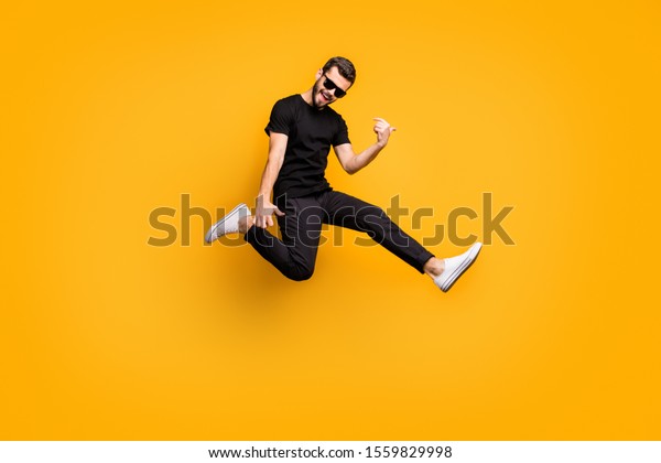 Full body profile photo
of crazy hipster guy jumping high holding imagine solo guitar music
lover wear sun specs black t-shirt pants isolated yellow color
background