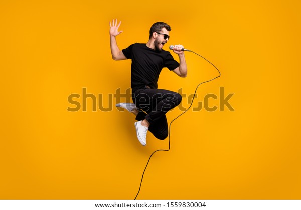 Full body\
profile photo of crazy hipster guy jumping high holding microphone\
music lover singing favorite song wear sun specs black t-shirt\
pants isolated yellow color\
background
